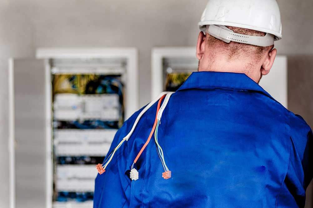 An electrician at work with a set of wires of their shoulder.