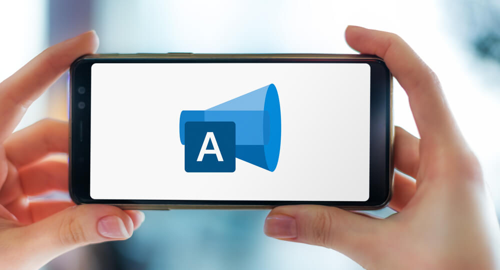 Hands holding smartphone displaying the Microsoft Advertising logo, a service that provides PPC advertising on both Bing and Yahoo!