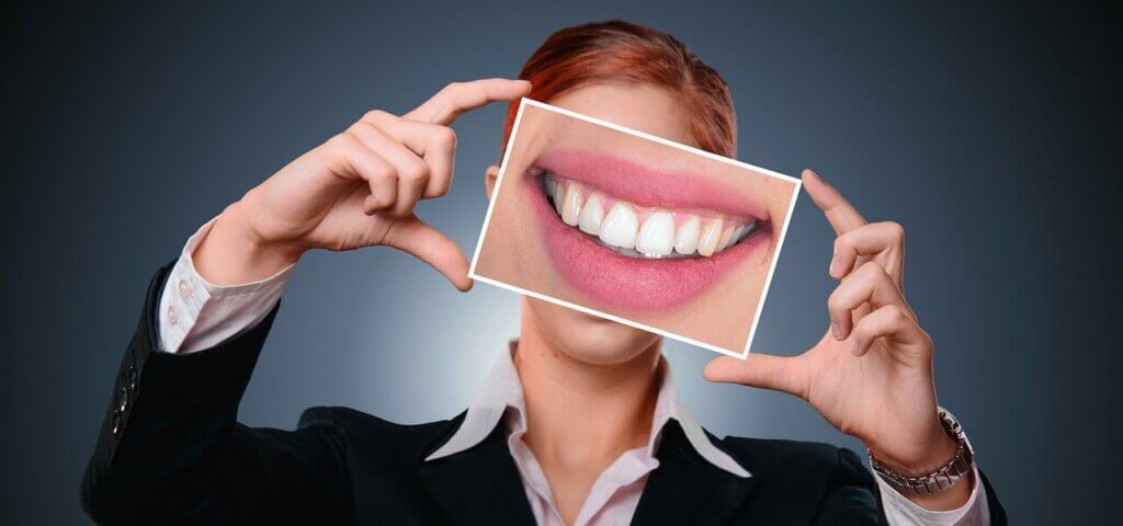 A well-dressed woman holding up a picture of her smile over her face.